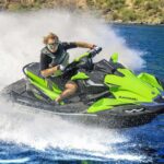 Person riding a green jet ski on a lake, creating splashes.