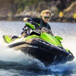 Person riding a green jet ski on water, creating splashes.