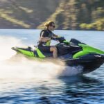 Person riding a green jet ski on water at high speed.
