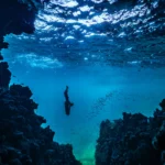 Underwater diver exploring a vibrant coral reef cave.