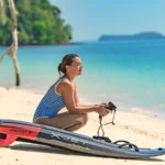 Woman sitting on a paddleboard at the beach, looking out at the ocean.