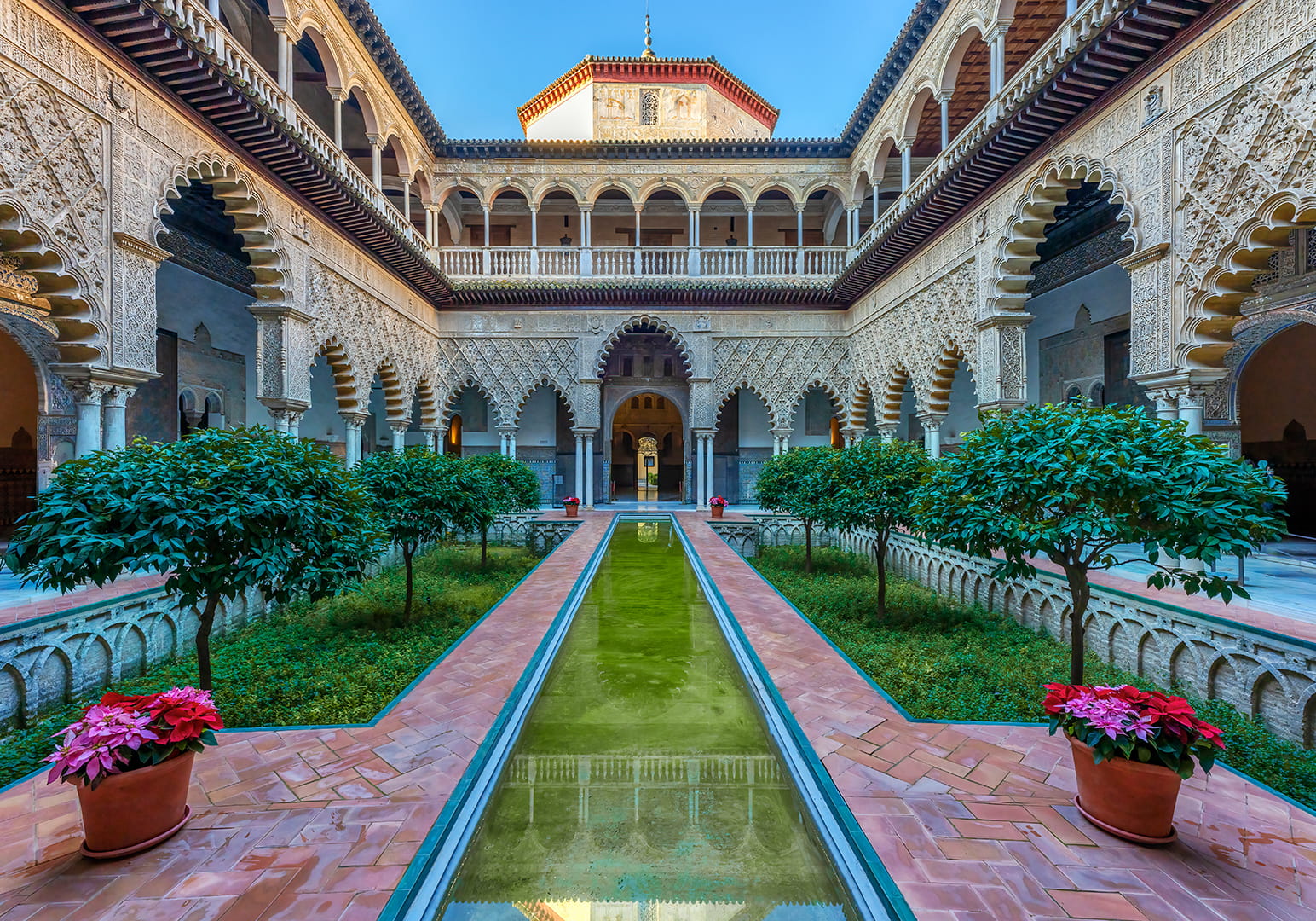 Ornate courtyard with arches, greenery, and a reflective water channel.