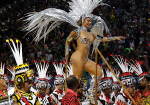 A performer in an elaborate feathered costume dances at a vibrant parade.