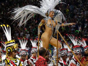 A performer in an elaborate feathered costume dances at a vibrant parade.