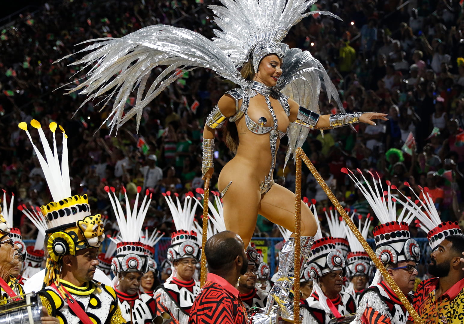 A performer in an elaborate feathered costume dances at a vibrant parade.