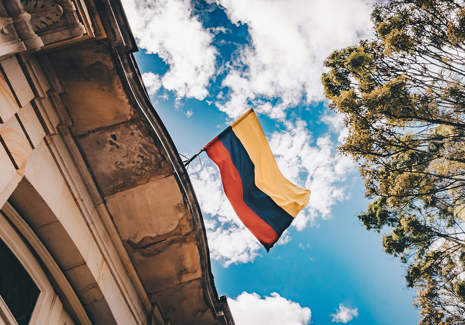 Colombian flag waving against a bright blue sky with clouds.