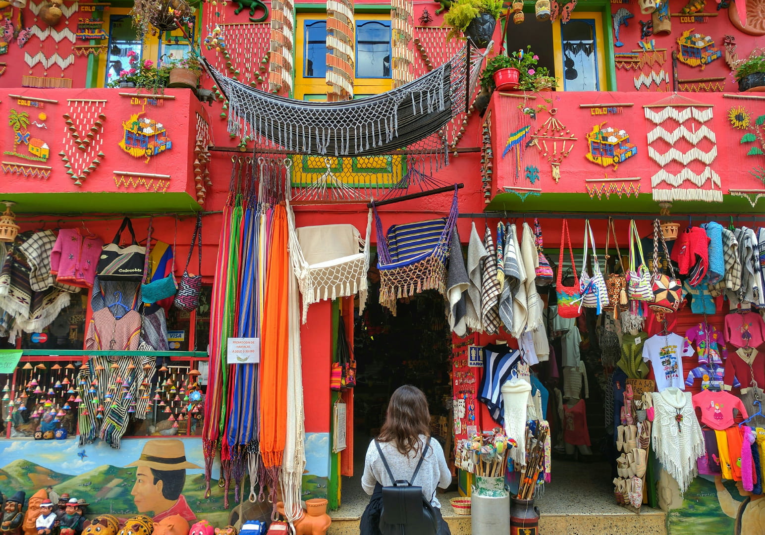 Colorful market entrance with textiles and souvenirs, and a woman observing.