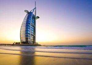 Burj Al Arab hotel standing tall at sunset by the beach.