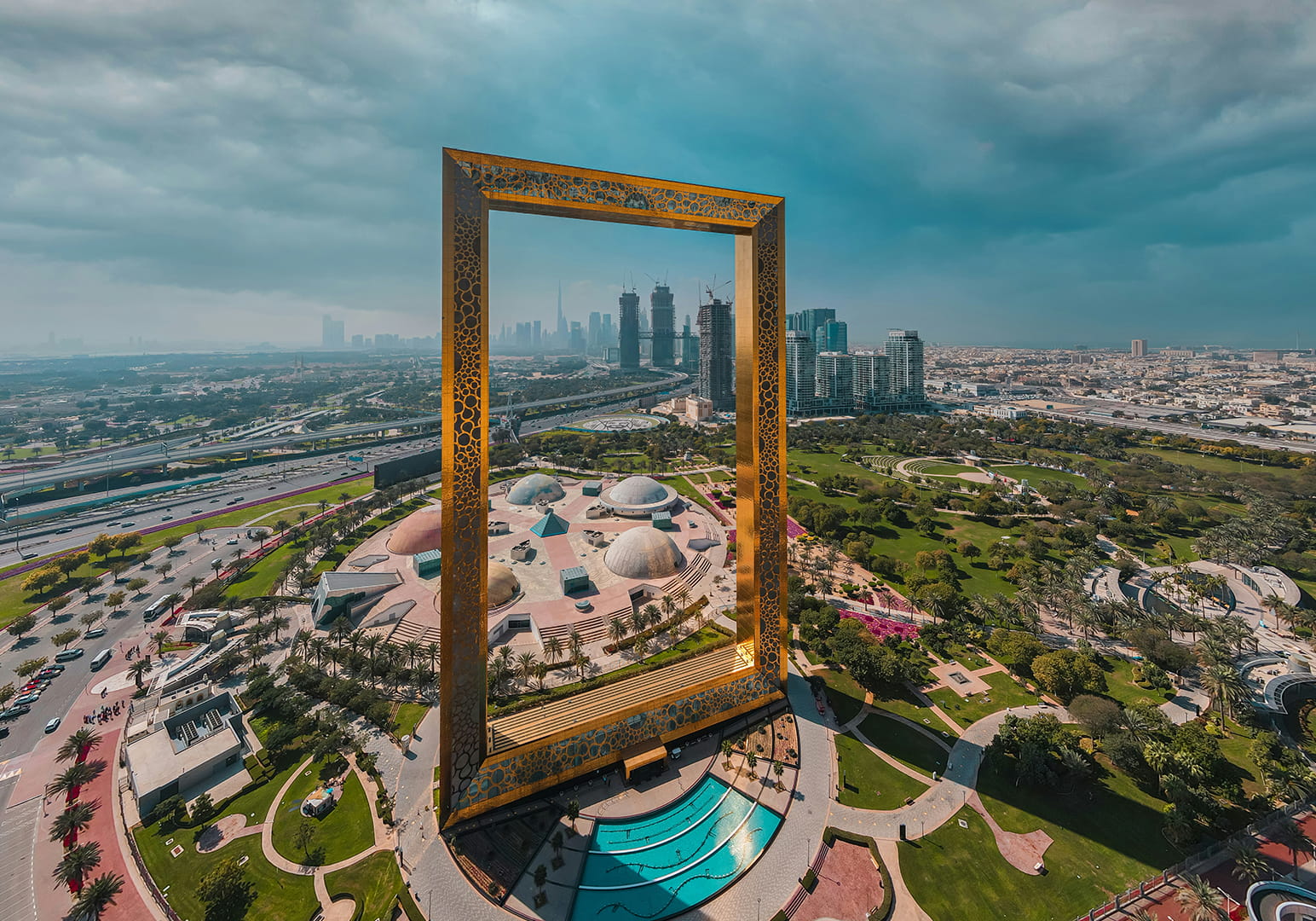 A giant golden picture frame overlooking a cityscape with skyscrapers and greenery.