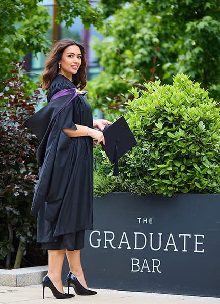 A woman in graduation gown holding a cap outdoors.